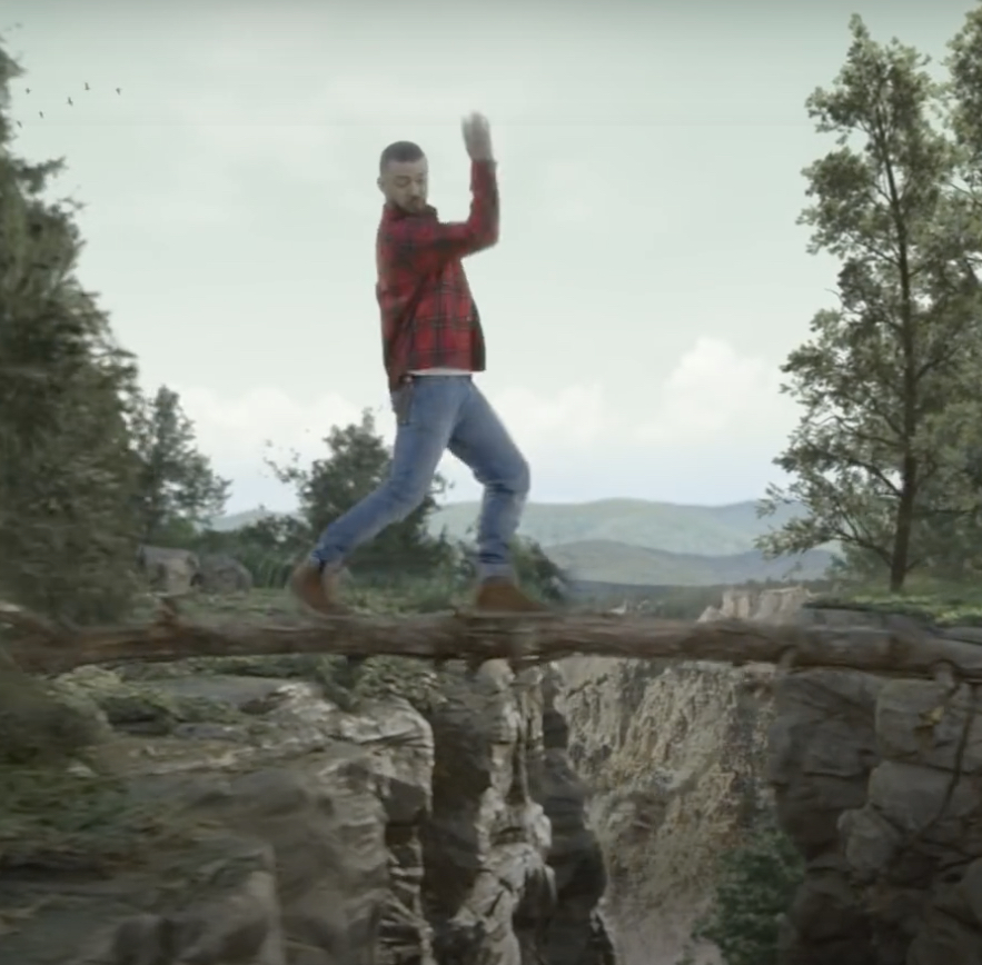 Screenshot from Justin Timberlake’s video, “Man of the Woods.” Timberlake is dancing on a log above a photoshopped ravine. Birds fly over mountains in the background.