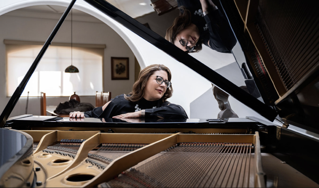 Composer Gabriela Ortiz seated at a grand piano with the lid open.